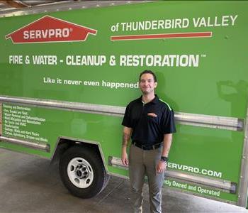 Male employee with brown hair smiling in front of a green SERVPRO truck
